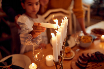 Close-up of daughter lights menorah candles during family meal on Hanukkah.
