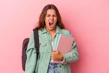 Fototapeta premium Young caucasian student woman holding books isolated on pink background screaming very angry and aggressive.