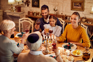 Happy Jewish extended family toasts at dining table while celebrating Hanukkah.
