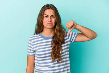 Young caucasian woman isolated on blue background  showing a dislike gesture, thumbs down....