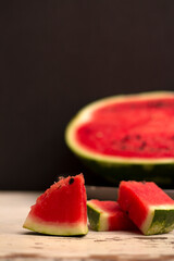 Food Photo of a slice of red juicy watermelon against the background of half a watermelon on an old wooden table against a dark background.
