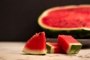 Food Photo of a slice of red juicy watermelon against the background of half a watermelon on an old wooden table against a dark background.
