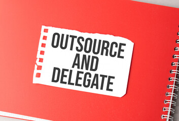 The word outsource and delegate on torn paper on red notepad,.