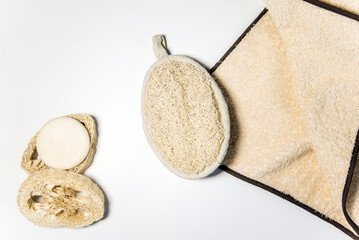 Esponja de lufa, dos discos cortados de lufa y un jabón sólido junto a una toalla de color beige sobre un fondo blanco. Concepto de desperdicio cero, sin plásticos - obrazy, fototapety, plakaty