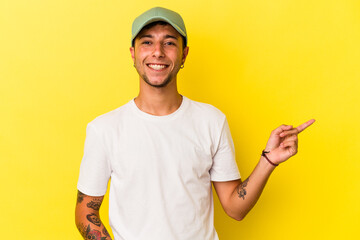 Young caucasian man with tattoos isolated on yellow background  smiling cheerfully pointing with forefinger away.