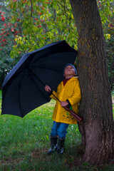 A boy walking under an umbrella in a yellow raincoat. Cloudy weather