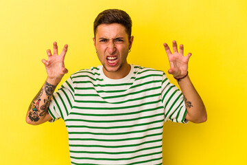 Young caucasian man with tattoos isolated on yellow background  upset screaming with tense hands.