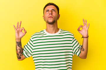 Young caucasian man with tattoos isolated on yellow background  relaxes after hard working day, she is performing yoga.