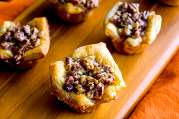 Pecan Pie Tartelettes Served on a Wooden Cutting Board: Individual pecan pie tarts displayed on a wood cutting board