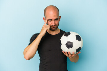 Young business bald man playing football isolated on blue background  pointing temple with finger, thinking, focused on a task.