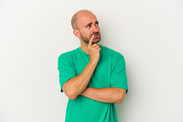 Young bald man isolated on white background looking sideways with doubtful and skeptical expression.