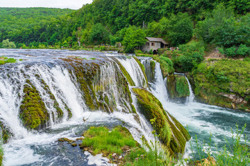 Fototapeta na wymiar A beautiful waterfall with a water mill and pure flowing water.