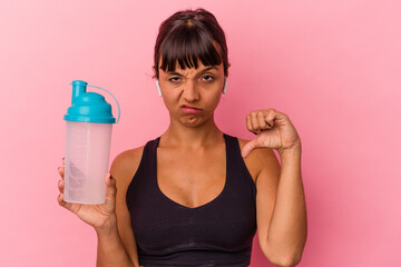 Young mixed race woman drinking protein shake isolated on pink background showing a dislike...