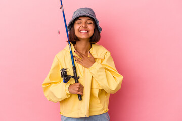 Young mixed race woman practicing fishing isolated on pink background laughs out loudly keeping hand on chest.