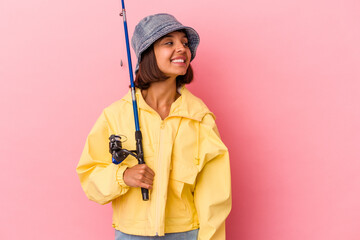 Young mixed race woman practicing fishing isolated on pink background looks aside smiling, cheerful and pleasant.