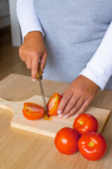 woman cutting a tomato in the middle on a wooden cutting board