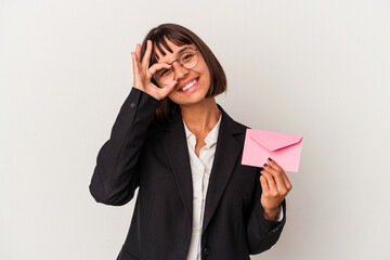Young mixed race business woman holding a letter isolated on white background excited keeping ok...