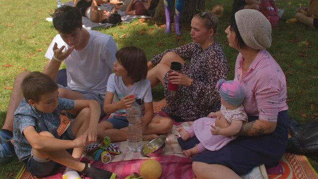 Picnic at free time company relaxing Kids choose healthy food in form fruits, drink clean water from plastic bottle. Communication between adults children their free time. 