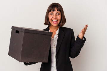 Young mixed race business woman holding a box isolated on white background receiving a pleasant...