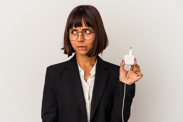 Young mixed race business woman holding a phone charger isolated on white background is saying a...