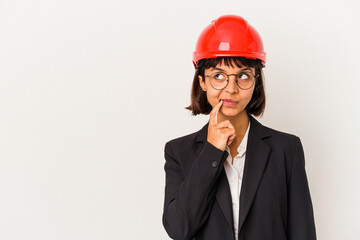 Young architect woman with red helmet isolated on white background looking sideways with doubtful and skeptical expression.