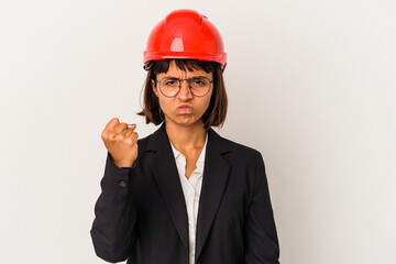 Young architect woman with red helmet isolated on white background showing fist to camera, aggressive facial expression.