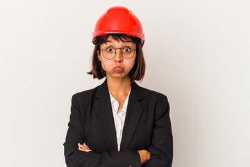 Young architect woman with red helmet isolated on white background blows cheeks, has tired expression. Facial expression concept.