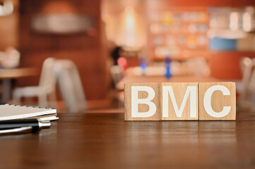 On a wood board, wooden word cubes are arranged in the letters BMC. It is an abbreviation for Business Model Canvas.