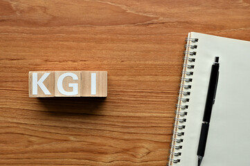 On a wood board, wooden word cubes are arranged in the letters KGI. It is an abbreviation for Key Goal Indicator.