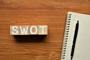 On a wood board, wooden word cubes are arranged in the letters SWOT. It is an abbreviation for Strength, Weakness, Opportunity, Threat.