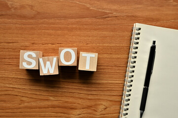 On a wood board, wooden word cubes are arranged in the letters SWOT. It is an abbreviation for Strength, Weakness, Opportunity, Threat.
