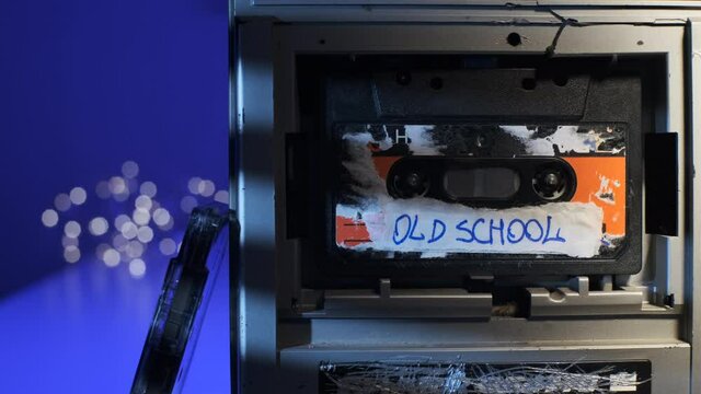 OLD SCHOOL sign on audio cassette label, which is played in old retro broken silver turntable. Music player close-up dolly view with cassette inserted.