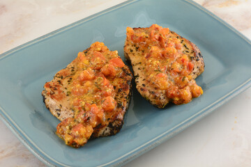 Two boneless pork chops with spicy tomato and red pepper sauce on blue serving plate