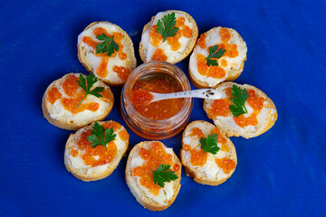 baguette croutons with butter and salmon caviar on blue plate, top view.