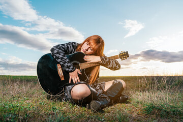 Woman sitting in a park hugging her black guitar under cloudy sky. - obrazy, fototapety, plakaty