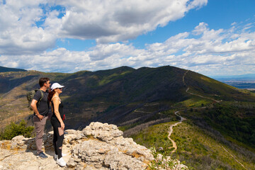  woman and man on a hike stand on the top of the mountain and look into the distance
