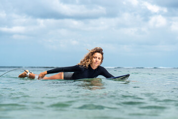 Portrait of surfer girl on white surf board in blue ocean pictured from the water