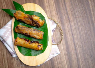 Piscok or Pisang Coklat, Chocolate Banana Crispy, Indonesian food on wooden cutting board decorated with bananas leaf