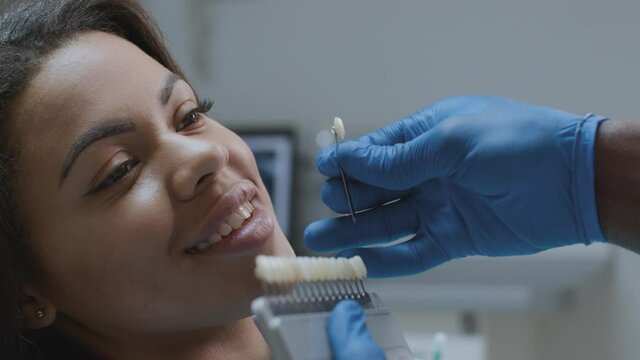 Dentist choosing right enamel color for african american female patient during medical treatment in modern dental clinic