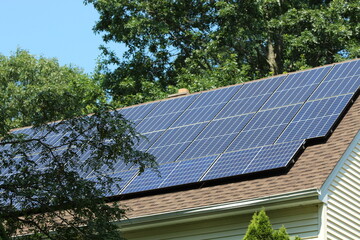 Solar panels on top of a house roof on a sunny summer day with blue sky and trees in the background
