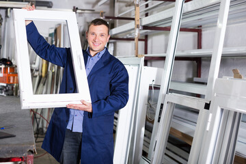 Smiling young professional labours with finished PVC profiles and windows at factory