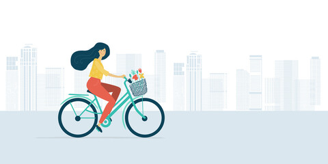Fototapeta premium Woman riding bicycle with basket of flowers. Cityscape background