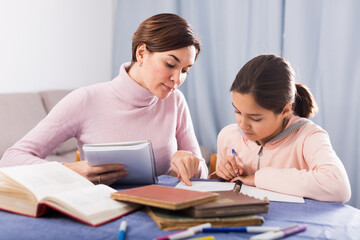 Fototapeta na wymiar Young mother and daughter are doing school homework together at home