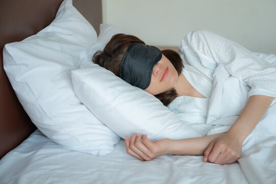 Portrait Of Young Beautiful Woman Wearing Sleep Mask During Sleeping On The Bed. A Sleep Mask Can Block Out Light When Sleeping, Allows The User To Achieve A Deeper Level Of Sleep.