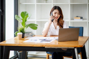 Portrait of Asian young female Businesswoman working on laptop computer doing finances,accounting analysis,report,data and pointing graph at the office.