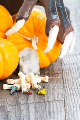 Halloween concept with miniature people, pumpkins, tombstone, bones candy and bony hand with long...
