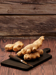 Ginger root and a knife on a burned wood cutting board over brown wood background