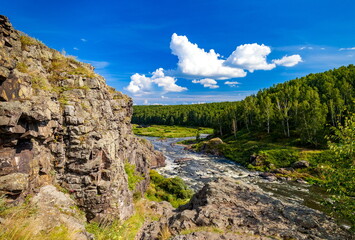 Fast river with rocky banks, overgrown with trees in summer