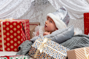 portrait of a cute little girl child wearing a silver color Christmas hat lying between gift boxes