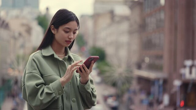 Asian woman holding cell phone while standing outdoors